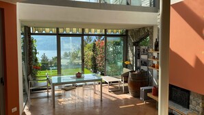 A spacious room with a large glass window, a dining table, chairs, a fireplace, and a stone wall. - Casa Leòn Lake View (Verbania)