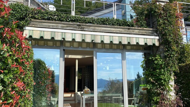 A modern house with a glass conservatory, a dining area, and a garden with a cat statue. - Casa Leòn Lake View (Verbania)