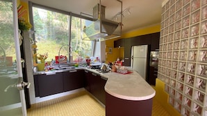 A modern kitchen with a central island, a built-in oven, and a large window providing a view of greenery outside. - Casa Leòn Lake View (Verbania)