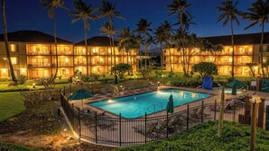 Un hôtel doté d’une piscine, de palmiers et d’un espace extérieur bien éclairé.