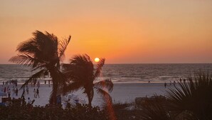A beach scene with palm trees, a sunset, and people walking along the shore.