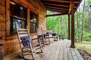 Una cabaña de madera con porche, mecedoras y vistas al bosque.