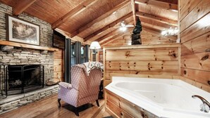 A log cabin interior with a stone fireplace, a large wooden bathtub, and a cozy armchair. - Peekaboo - Hot Tub, Pool Table, and Jacuzzi! (Sevierville)