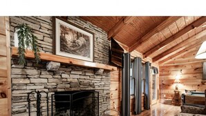A cozy log cabin interior with a stone fireplace, wooden beams, and a comfortable seating area. - Peekaboo - Hot Tub, Pool Table, and Jacuzzi! (Sevierville)