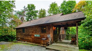 A rustic wooden cabin with a porch, a gravel driveway, and signs indicating its location. - Peekaboo - Hot Tub, Pool Table, and Jacuzzi! (Sevierville)