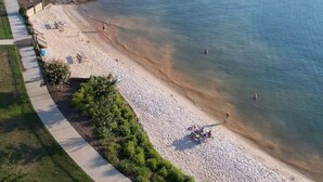 Ein Strand mit befestigtem Gehweg, klarem Wasser und einigen Personen.
