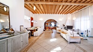 Un vaste espace de vie doté d’un haut plafond en bois, un coin repas avec une longue table, et un espace détente avec un canapé et des fauteuils.