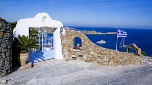 Un bâtiment situé sur la côte, doté d’un mur en pierre, d’une entrée blanche et offrant une vue sur la mer.