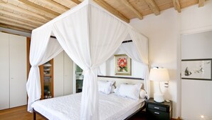 Une chambre à coucher avec un lit à baldaquin, un plancher en bois, une table de chevet avec une lampe et un tableau encadré au mur.