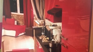 A compact kitchen with red cabinets, a dining area with a red sofa, and a window with curtains. - 2P FRONT DE NEIGE SUD CALME (Isola)