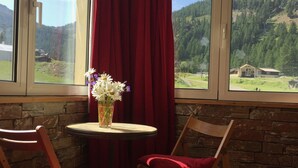 A room with a table and two chairs, a vase with flowers, and a view of a mountainous landscape through large windows. - 2P FRONT DE NEIGE SUD CALME (Isola)