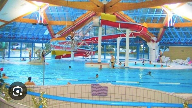 An indoor swimming pool with a high ceiling and wooden beams, featuring multiple lanes and water slides. - 2P FRONT DE NEIGE SUD CALME (Isola)