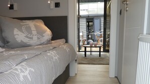 Ein Schlafzimmer mit Bett, Nachttischlampen und Blick in einen Essbereich mit Stühlen und Tisch.