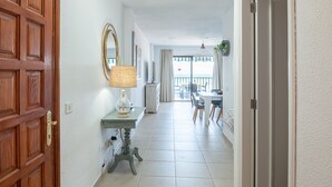 Un pasillo con una puerta de madera, una mesa con lámpara y vistas a un balcón con sillas.