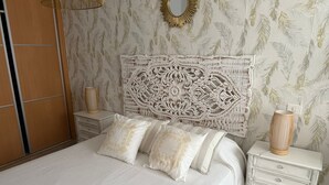 Un dormitorio con una cama grande, un cabecero decorativo, una mesita de noche con lámpara y un aparador.