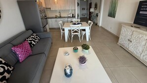 Una sala moderna con un sofá gris, una mesa de comedor blanca y una araña.