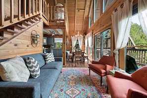 A wooden interior with a sofa, patterned rug, and a dining area.