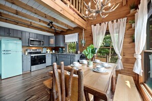 A rustic kitchen with wooden cabinets, a stainless steel refrigerator, and a dining area with a wooden table and chairs.