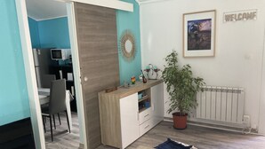 A modern living room with a wooden coffee table, a TV, and a sofa. There's a door leading to a dining area with a table and chairs. A potted plant is on the floor, and a welcome sign is on the wall. - Charming countryside home with a private garden (Le Beausset)