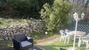 An outdoor patio area with wicker furniture, a stone wall, and a lawn. - Charming countryside home with a private garden (Le Beausset)