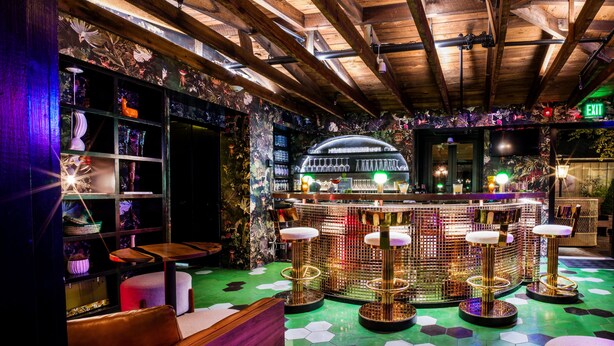 Una zona de bar con vigas de madera, suelo de baldosas verdes y una barra con taburetes.