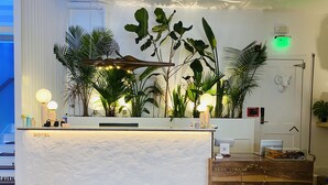Un comptoir d’accueil d’hôtel avec un plan de travail blanc, un bureau d’accueil en bois et un panneau de signalisation de sortie vert.