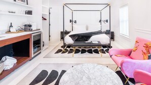 Une chambre d’hôtel moderne avec un lit à baldaquin, un bureau avec un ordinateur, un fauteuil rose et une table basse en marbre.