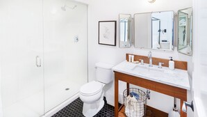 Une salle de bain moderne dotée d’une douche à parois de verre, de toilettes, d’un lavabo avec un meuble-vasque en bois et d’un miroir à trois panneaux.