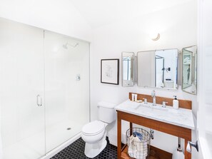 A modern bathroom with a glass shower enclosure, a toilet, a sink with a wooden vanity, and a mirror with three panels.