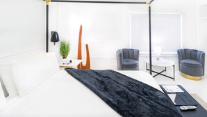 A modern bedroom with a four-poster bed, two armchairs, a small table, and a potted plant.