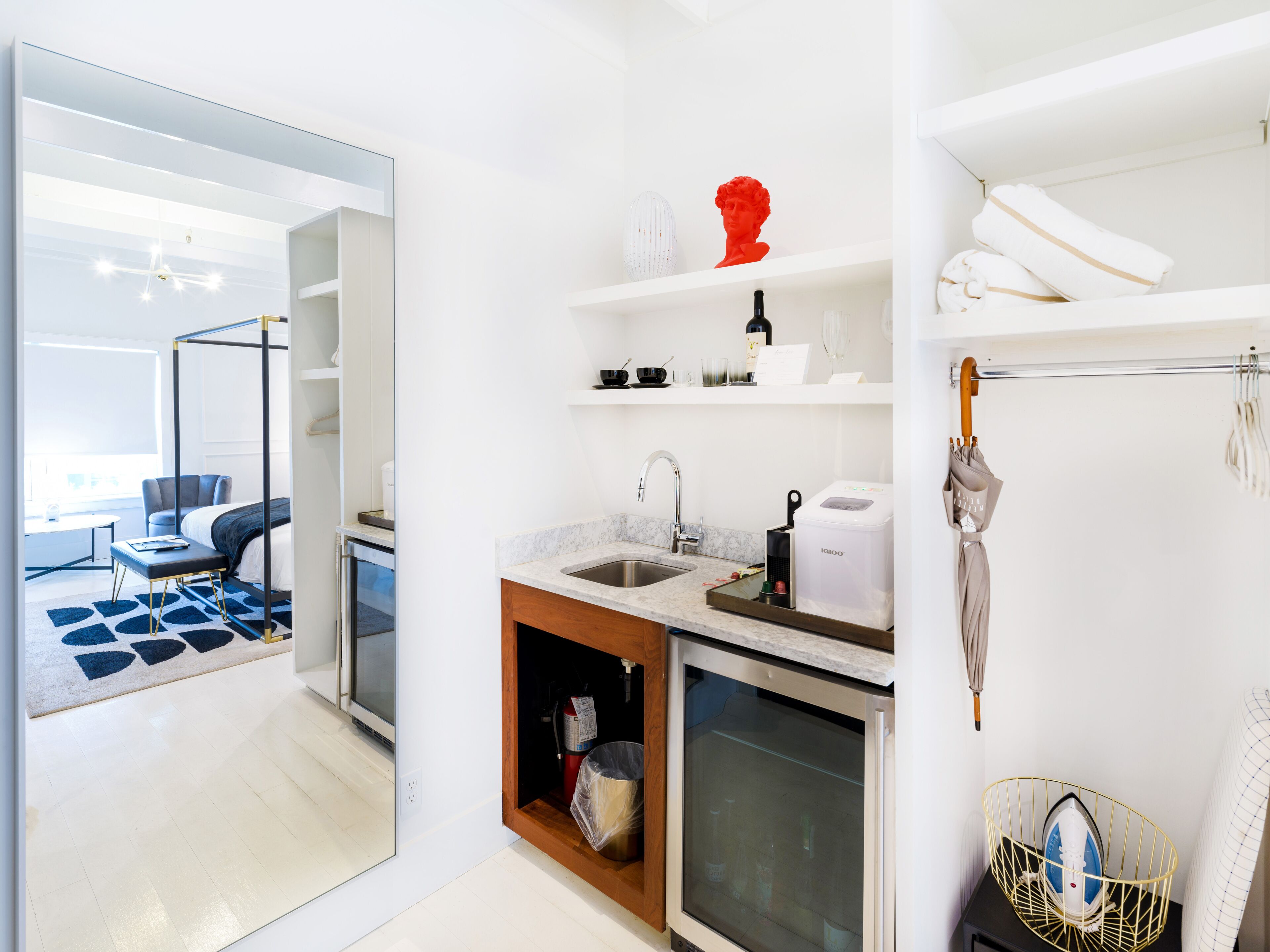 Een moderne hotelkamer met een balkon, een kitchenette, een grote spiegel en een keurig opgeruimde badkamer.