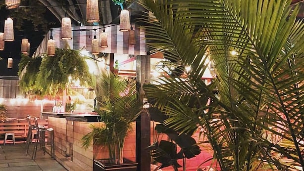 Un área de comedor al aire libre con luces colgantes, palmeras y un bar.