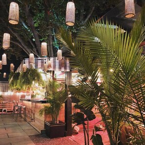 Un espace extérieur aménagé pour les repas, avec des guirlandes lumineuses, des palmiers et un bar.