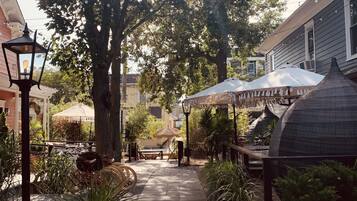 A paved walkway lined with potted plants and a thatched-roof table under a string of lights.
