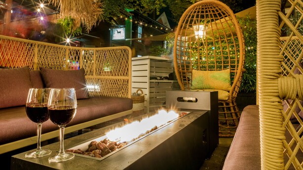 An outdoor seating area with wicker furniture, a fire feature, and glasses of red wine. - American Beech in Greenport - Two-Bedroom Apartment 8 (Greenport)