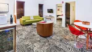 A modern living room with a green sofa, a wooden coffee table, and a zebra-patterned floor. There is a TV mounted on the wall, a small table with a red bowl, and a door leading to another room. - American Beech in Greenport - Two-Bedroom Apartment 8 (Greenport)