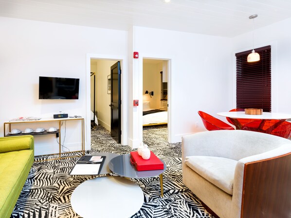 Una habitación de hotel moderna con suelo estampado de cebra, un televisor de pantalla plana, un sofá, una silla roja y una mesita con un cuenco.