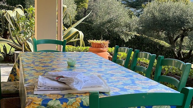Une terrasse extérieure avec une table recouverte d’une nappe à motifs de tournesols, entourée de chaises vertes.