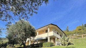 Une maison à deux étages dotée d’un balcon, entourée d’une pelouse bien entretenue et d’arbres.