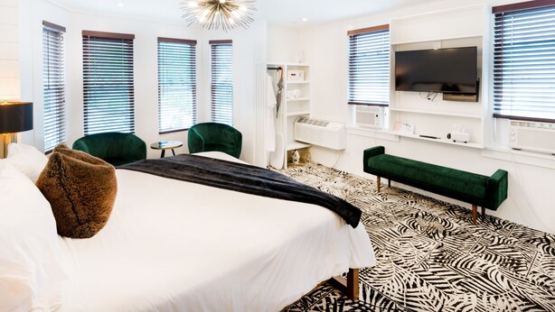 Una camera d'albergo moderna con un letto grande, poltrone verdi, un divano verde, una televisione e un pavimento decorato.