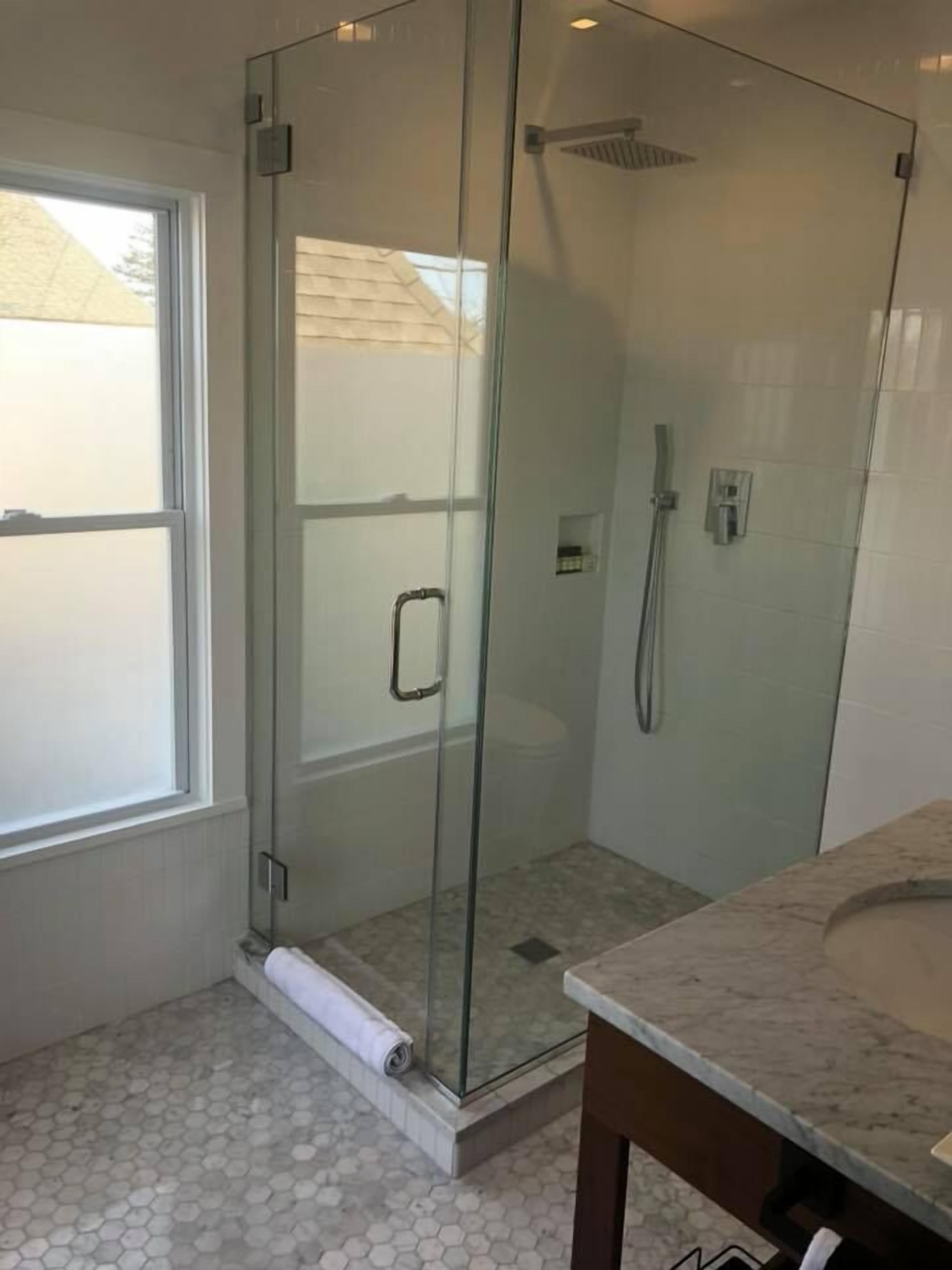A modern bathroom with a glass shower enclosure, a marble countertop, and a hexagonal tile floor.