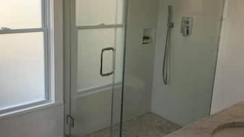 A modern bathroom with a glass shower enclosure, a marble countertop, and a hexagonal tile floor.