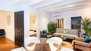 A modern living room with a glass table, white chairs, a sofa, and a coffee table. - American Beech - Luxury 2 Bedroom Apartment 10 (Greenport)
