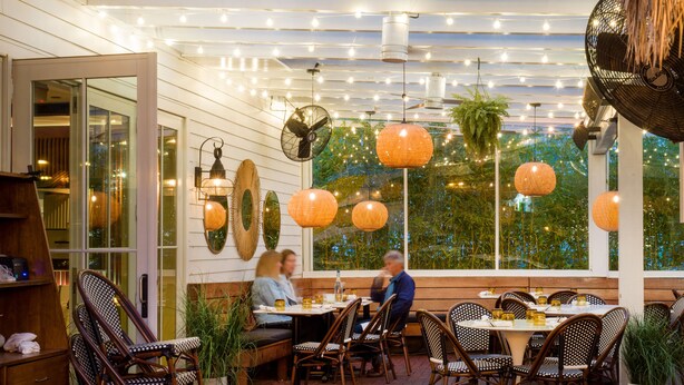 Un área de comedor al aire libre con mesas y sillas, luces colgantes y faroles.