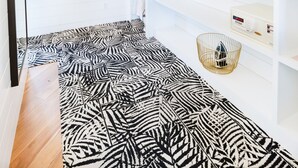 A room with a zebra-patterned rug, wooden beams on the ceiling, a white wall with a colorful abstract painting, and a white shelf with various items.