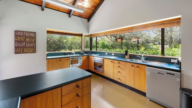 A modern kitchen with wooden cabinets, a black countertop, and a view of greenery outside.