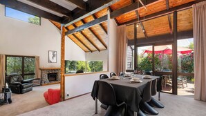 A modern dining area with a large table set for six, a fireplace, and a view of the outdoors.