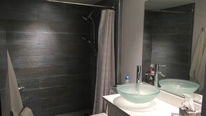Ein modernes Badezimmer mit dunklen Fliesen, einem Waschbecken aus Glas, einer Duschkabine mit Vorhang und einer Toilette.