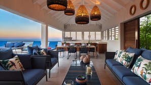 Une pièce spacieuse offrant une vue sur l’océan, comprenant un coin repas avec des chaises et une table, ainsi qu’un coin salon avec des canapés et une table basse.