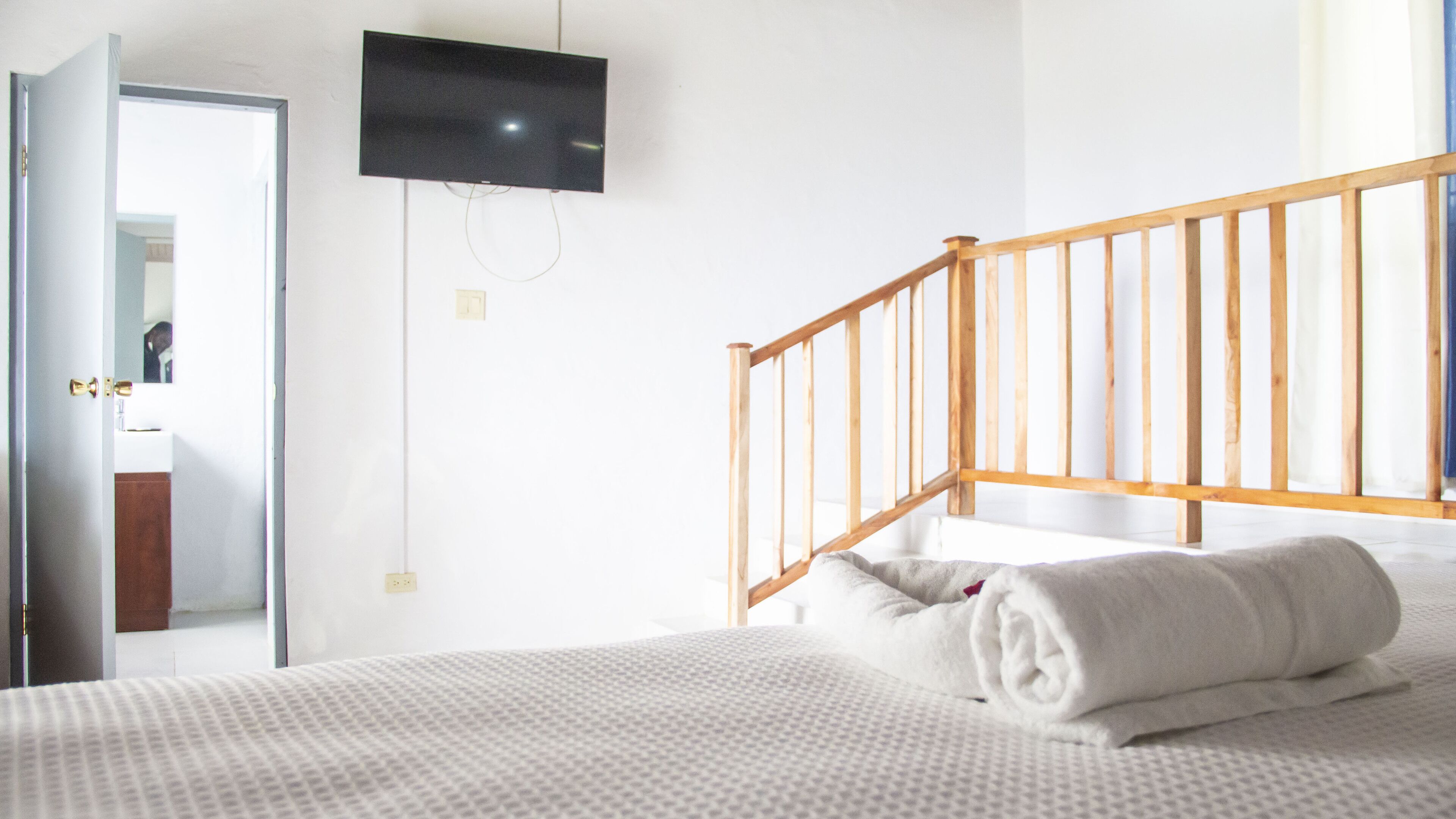 Un dormitorio con cama, una escalera de madera, un televisor montado en la pared y una puerta que da al baño.